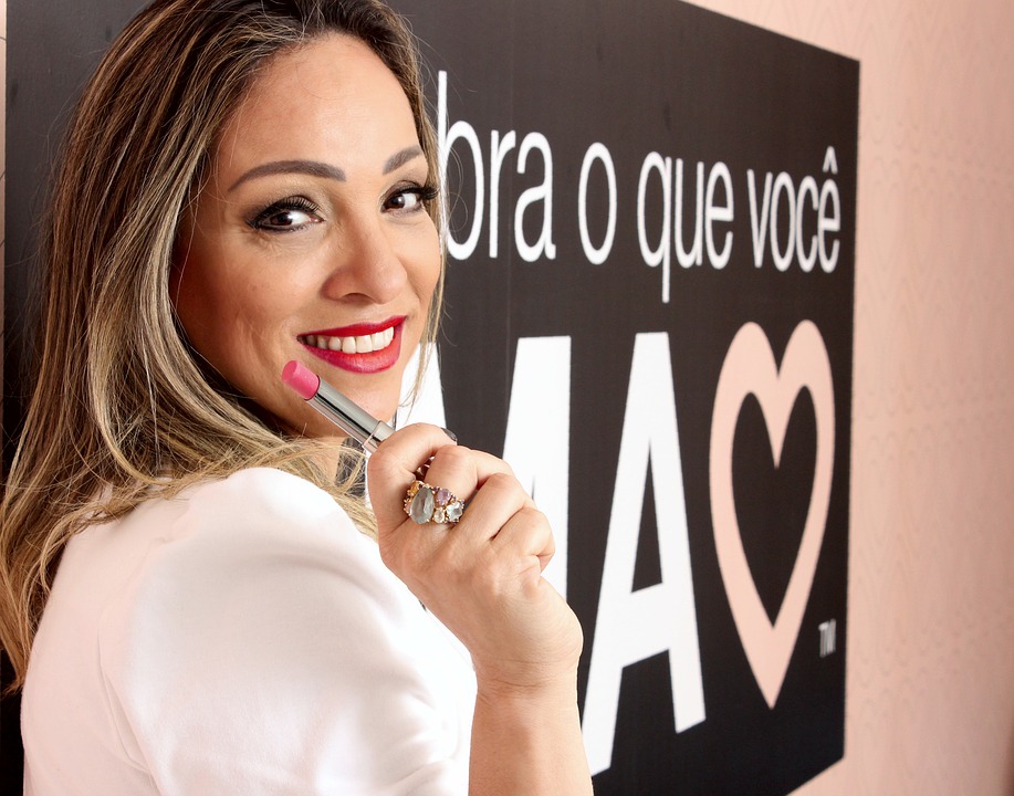 blone girl smiling with a lipstick on her hand